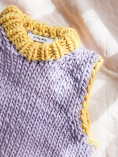 a purple and yellow knitted sweater laying on top of a white sheet with a tag