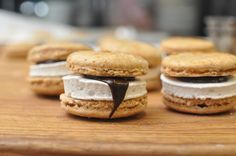 several cookies with cream and chocolate fillings on a wooden table next to a glass of water