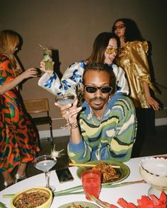 a group of people standing around a table with food and drinks in front of them