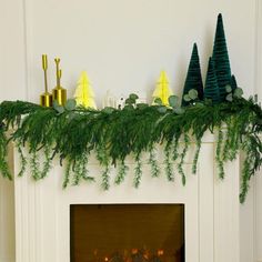 a fireplace decorated for christmas with candles and evergreen garland