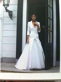 a woman in a white wedding dress standing on the front steps of a house with an open door