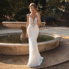 a woman standing in front of a fountain wearing a wedding dress with an open back