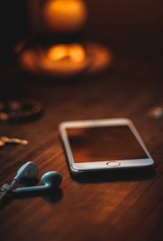 a cell phone sitting on top of a wooden table next to ear buds and candles