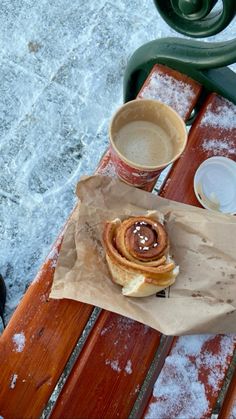 a cup of coffee sitting on top of a wooden bench next to a cinnamon roll