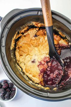 a crock pot filled with blueberry cobbler filling and topped with a wooden spoon