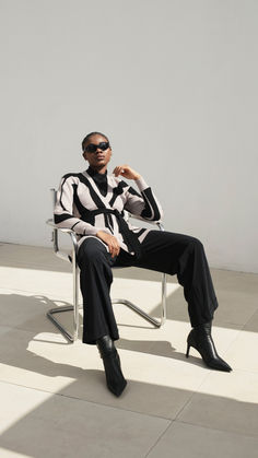 a man sitting in a chair with his hand on his hip wearing sunglasses and a striped shirt