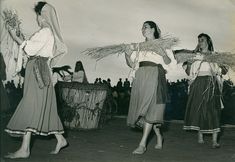 three women in long skirts are standing on the stage and one woman is holding grass