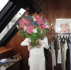 a woman holding a vase filled with lots of flowers