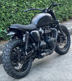 a black motorcycle parked on the street next to some bushes