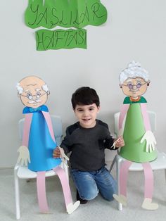 a young boy sitting in front of three paper sculptures that look like people with hands on their hipss