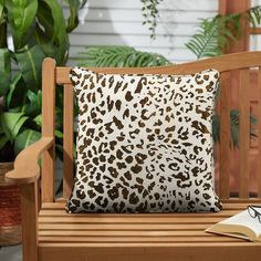 a leopard print pillow sitting on top of a wooden bench next to potted plants