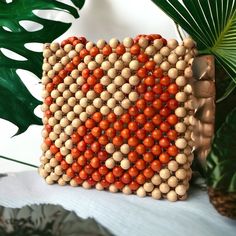 an orange and white beaded purse sitting on top of a table next to a plant