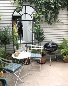 a patio with chairs, table and potted plants on the side of the house