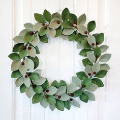 a wreath made out of green leaves and red berries hanging on a white door frame