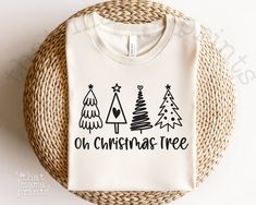 a t - shirt with the words oh christmas tree printed on it sitting next to a wicker basket