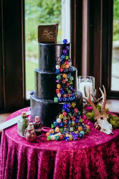 a three tiered black cake with colorful candies on the side and deer antlers