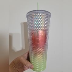 a person holding up a cup with a lid and straw in front of a white wall