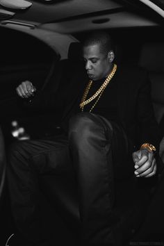 a man sitting in the back seat of a car wearing a gold chain on his neck