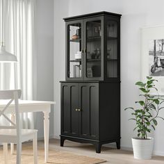 a black china cabinet with glass doors in a white dining room setting next to a potted plant