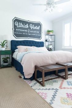 a bedroom with white walls and blue bedding, rugs and a large sign on the wall