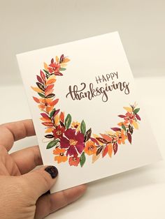 a hand holding a card with the words happy thanksgiving written on it and an autumn wreath