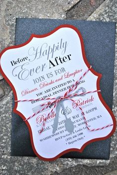 a black and white wedding card with red ribbon tied around the edge, on top of a stone slab