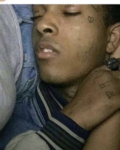 a close up of a person laying down with his eyes closed and tattoos on his face