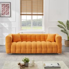 an orange couch sitting on top of a white rug in a living room next to a window