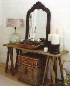 a wooden table topped with a mirror next to a basket filled with pine cones and candles