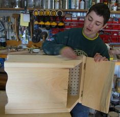 a young man working on a piece of furniture in a shop with lots of tools