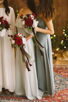 three bridesmaids in long dresses holding bouquets with red roses and greenery