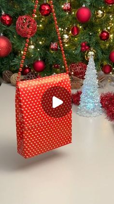 a red and white christmas present sitting on top of a table next to a tree