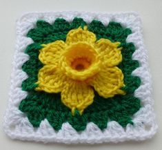 a crocheted square with a yellow flower on it and green leaves in the center