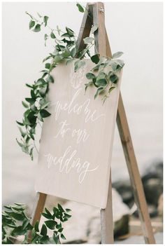 a wooden sign with greenery on it that says welcome to our wedding written in white