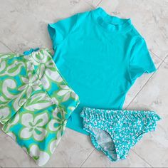 three children's swimsuits laying on the floor, one in blue and one in green