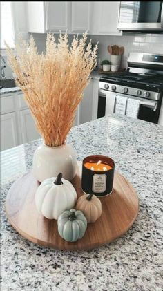 a candle and some pumpkins on a wooden tray in a kitchen with granite counter tops