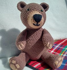 a brown teddy bear sitting on top of a plaid blanket