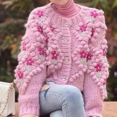 a woman sitting on top of a wooden table wearing a pink knitted sweater and jeans