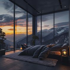 a person laying on a bed in front of large windows with mountains outside at sunset