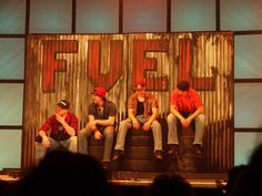 four young men sitting on top of a stage