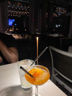 an orange cocktail in a martini glass on a table with a lit candle at the end