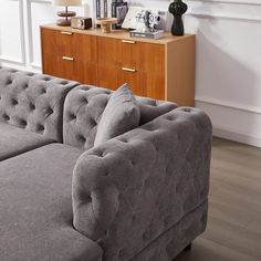 a gray couch sitting in front of a wooden dresser next to a window with white curtains