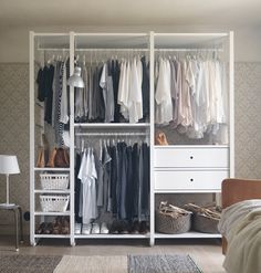 a white closet with clothes and baskets on the bottom shelf, next to a bed