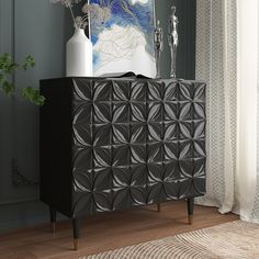 a black cabinet sitting in front of a window next to a vase with flowers on it