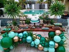 a table with balloons, plants and cake on it in front of a swimming pool