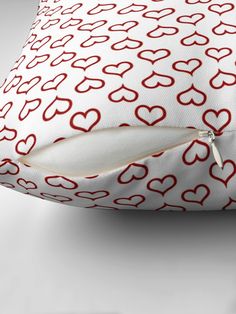 a red and white pillow with hearts on it's side, in front of a gray background