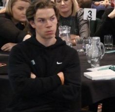 a man sitting at a table with his arms crossed in front of him, surrounded by other people