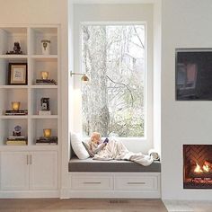 a person sitting on a window seat in front of a fire place with bookshelves