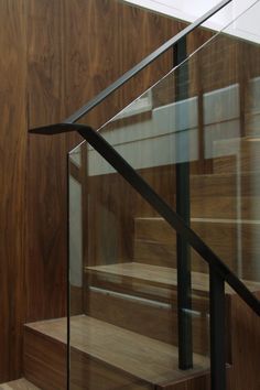 a glass handrail on the side of a stair case with wood paneling behind it