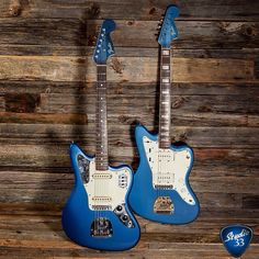 two electric guitars sitting on top of a wooden floor next to each other, one blue and the other white